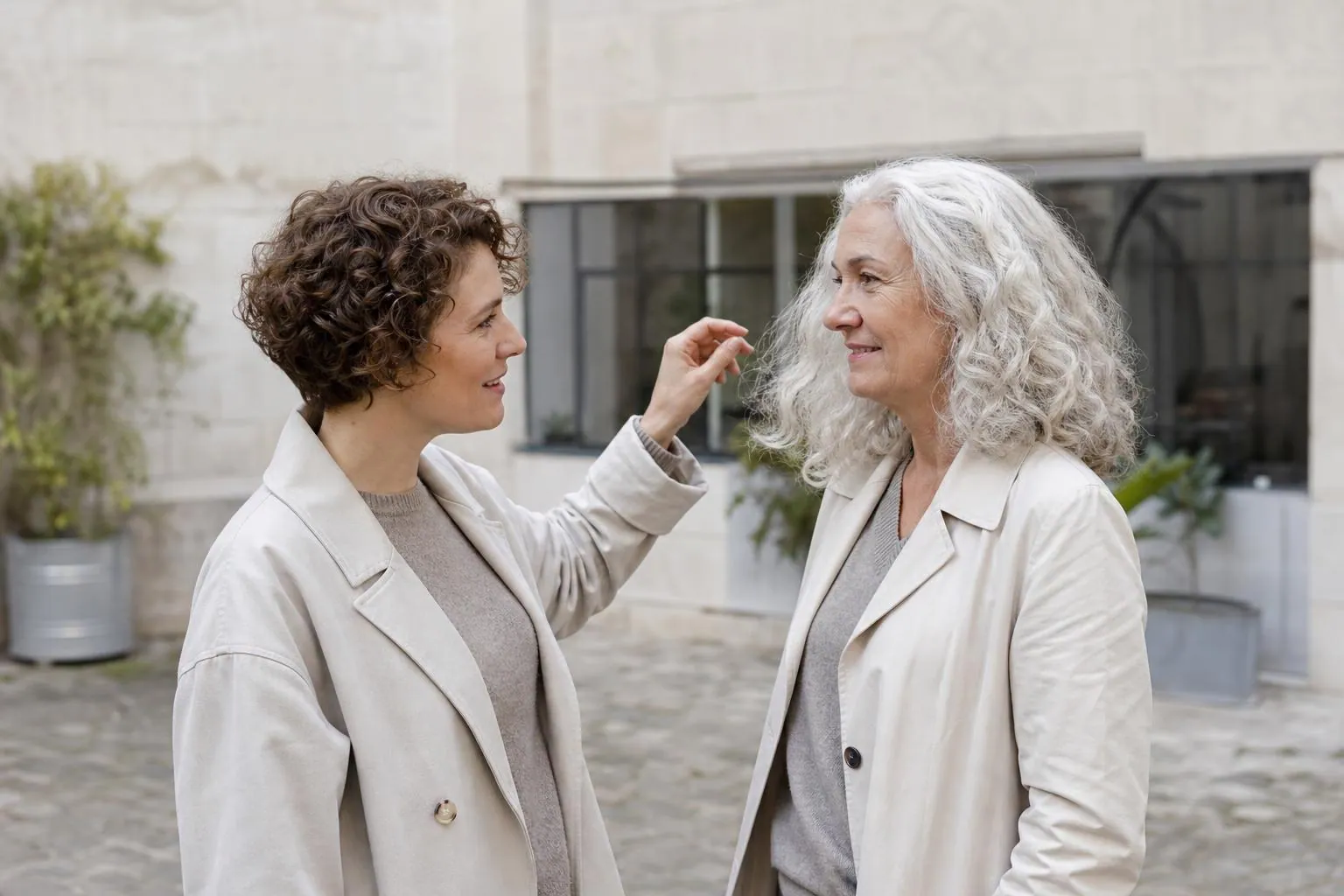 Deux femmes de générations proches, cheveux bouclés et frisés poivre et sel, discutant dans une cour d’immeuble parisienne